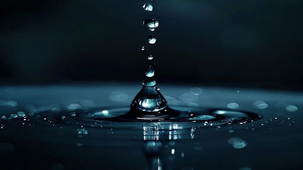 A single drop of clear liquid impacting a dark polished surface, ripples spreading outward